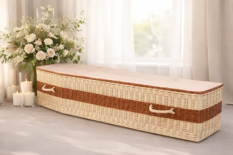 Cercueil en osier tressé disposé dans une pièce illuminée avec des fleurs.